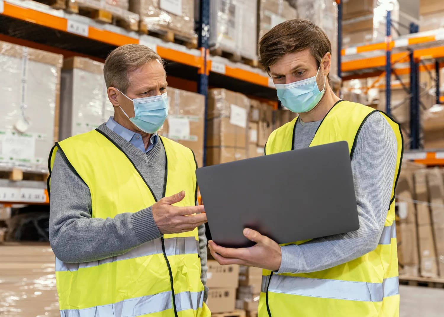 Logistics staff reviewing operations on a laptop in a warehouse